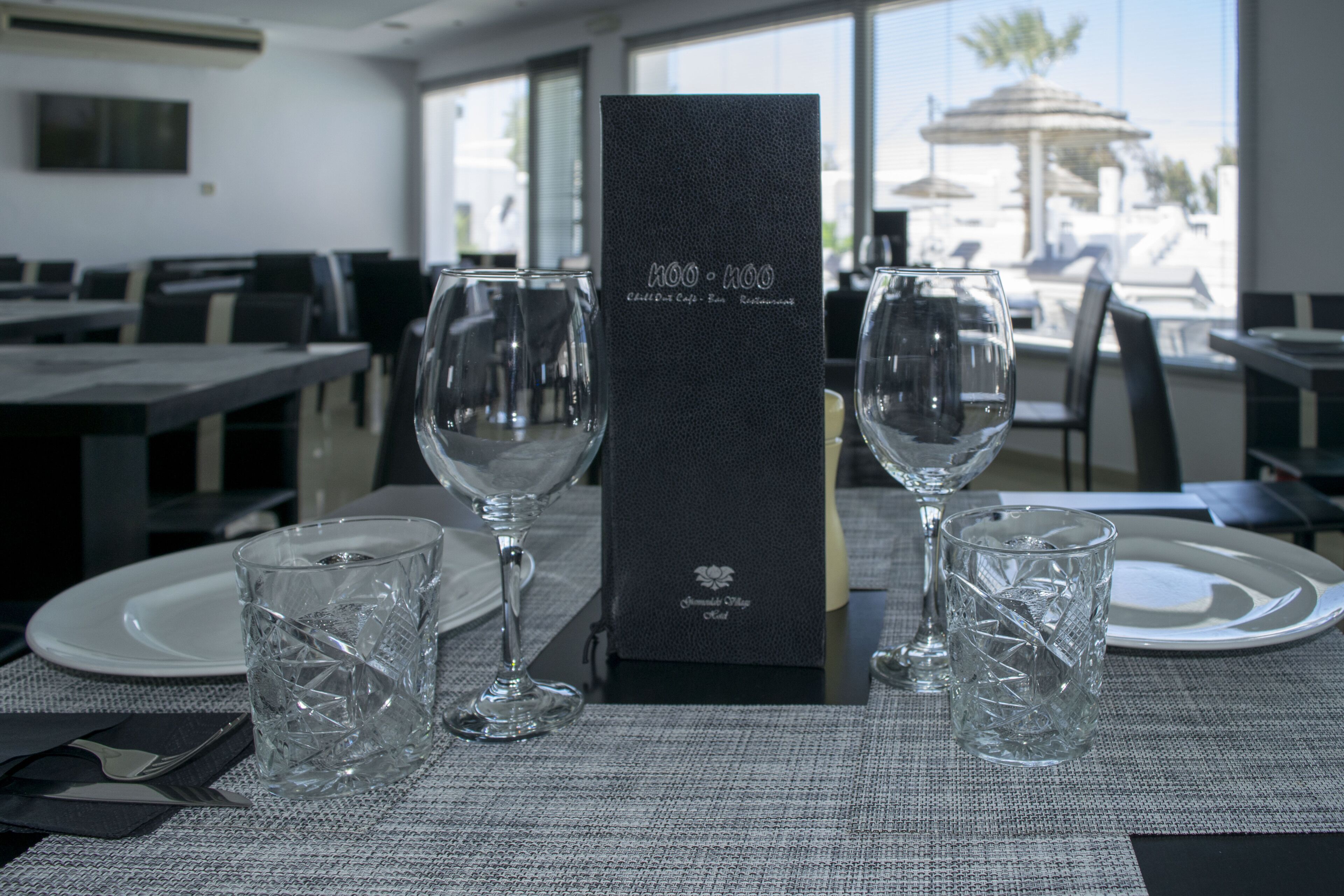 A dining table with two wine glasses, a menu, and a plate set for a meal.