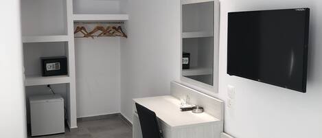 A modern, minimalistic room with a white desk, a black chair, a TV mounted on the wall, and a small refrigerator.