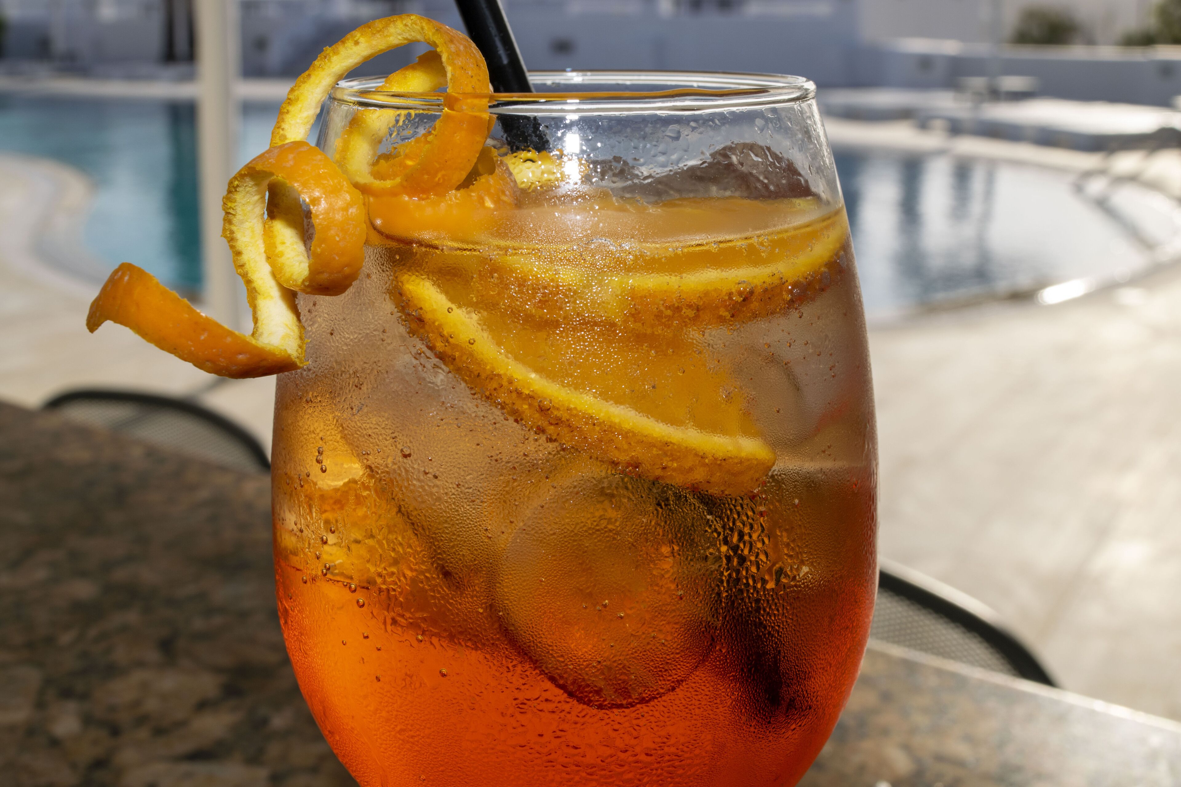 A glass of iced tea with lemon slices and a straw, placed on a table near a pool.