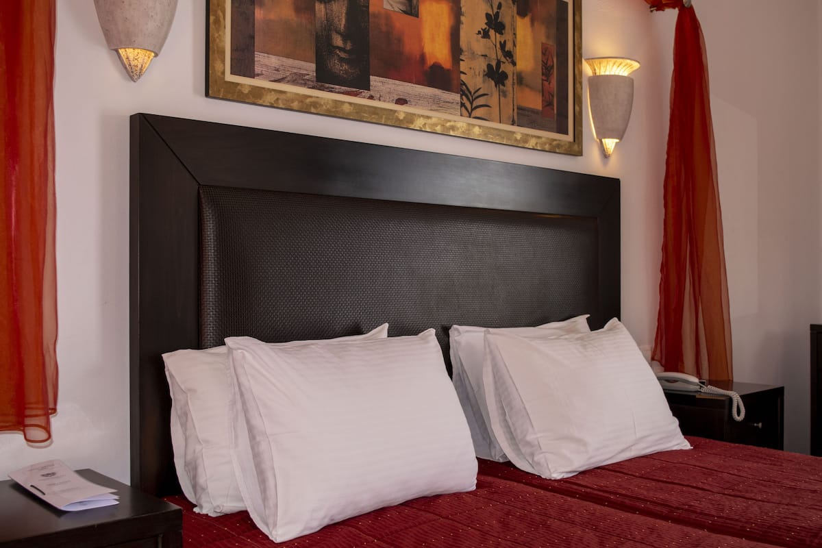 Een net opgemaakt bed met witte lakens, een donker hoofdbord en een schilderij erboven.