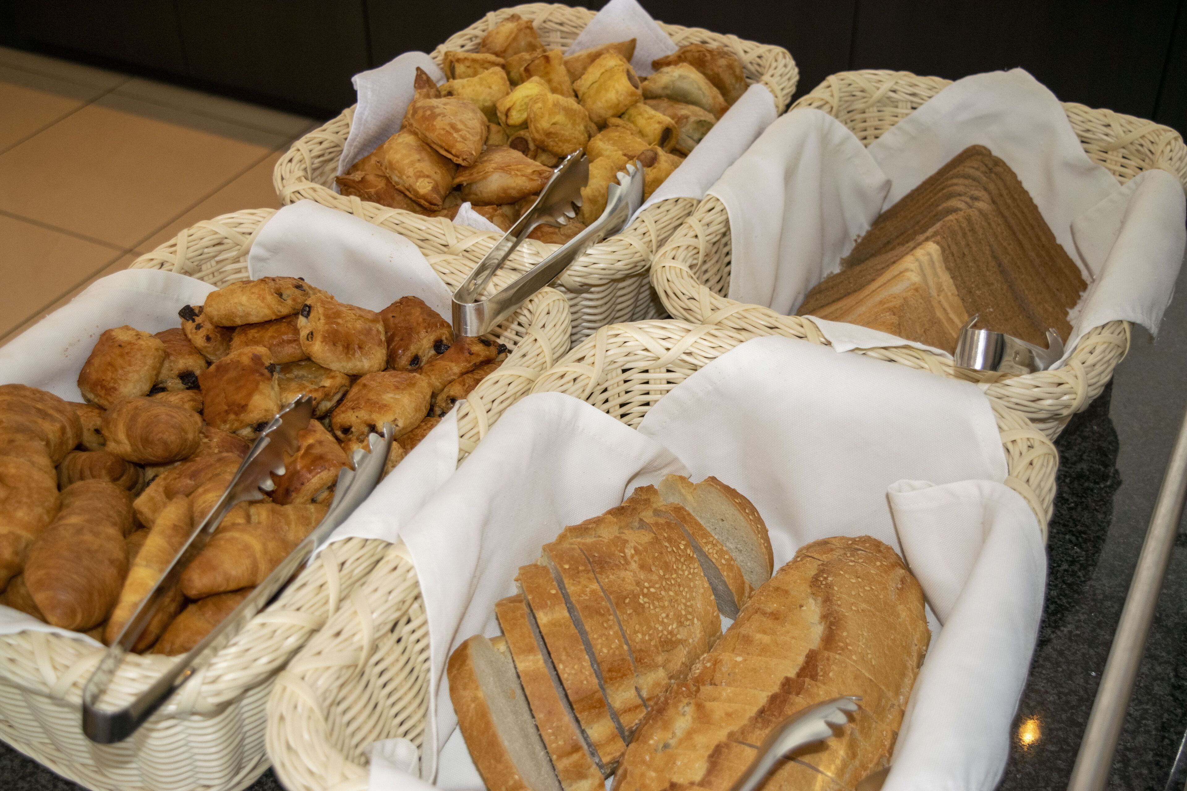 A buffet with various baked goods including croissants, pastries, and sliced bread.