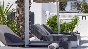 Un espace de détente extérieur, baigné de soleil, avec des fauteuils inclinables, un palmier et des plantes en pot.