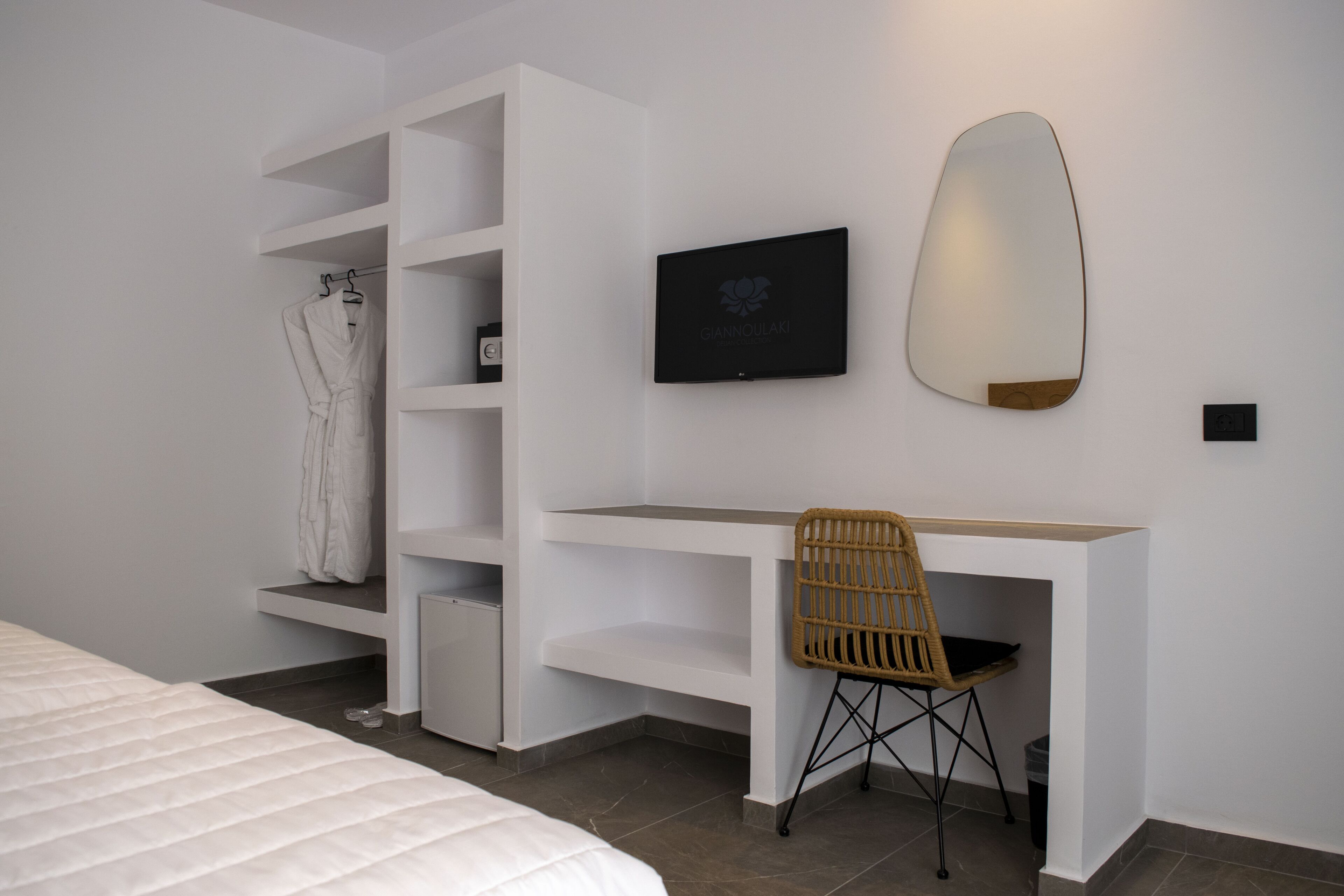 Un dormitorio moderno con una cama, un armario blanco, un escritorio con silla, un televisor de pantalla plana y un espejo montado en la pared.