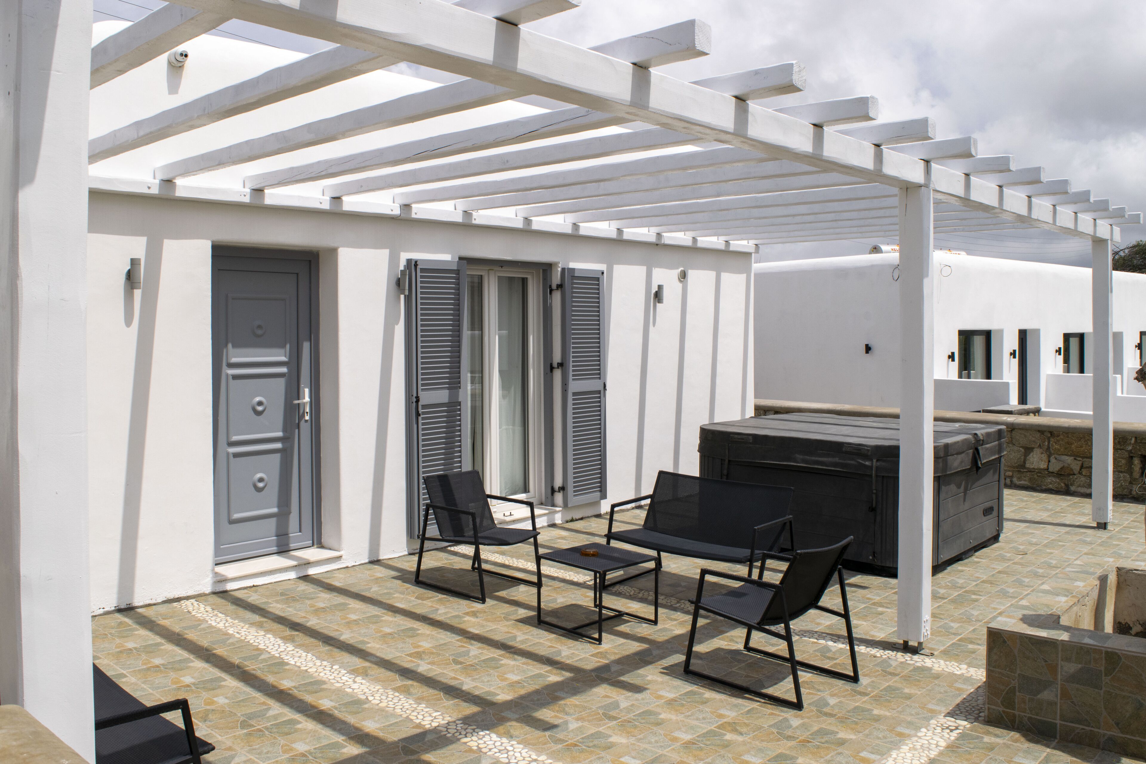 A covered outdoor seating area with a grill, two chairs, and a table.