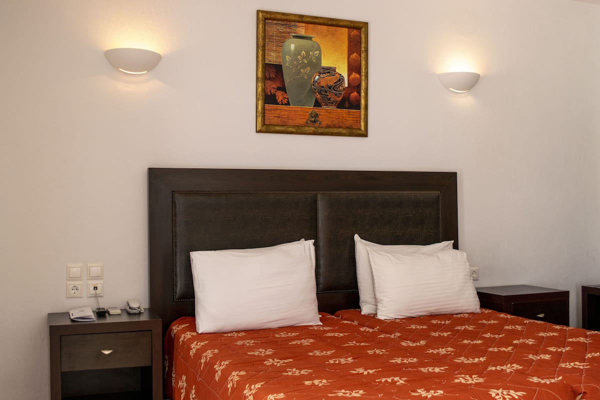 Een hotelkamer met een groot bed, twee nachtkastjes, een wandlamp en een schilderij aan de muur.