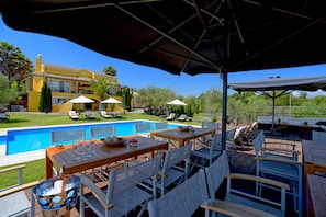 Un espace aménagé au bord de la piscine, avec une table en bois, des chaises en osier et des parasols.