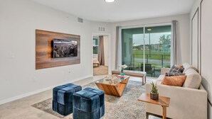 A modern living room with a large window, a cityscape painting, and a sofa with cushions. - 3bd/2ba condo close to Disney, Storey Lake (Kissimmee)