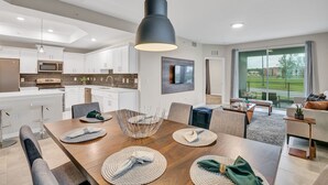 A modern kitchen with white cabinets, a large island, and a dining area with a wooden table and chairs. - 3bd/2ba condo close to Disney, Storey Lake (Kissimmee)