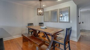 Un comedor con una mesa de madera, cuatro sillas, un banco y una araña.