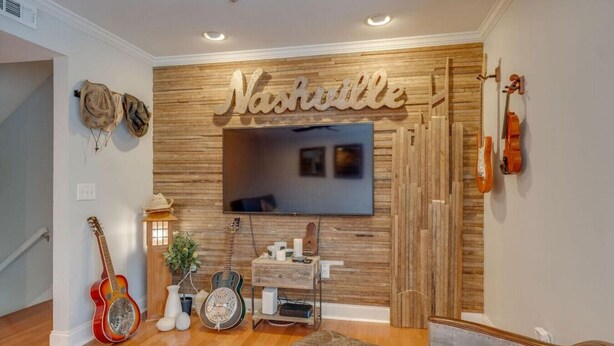 Una habitación con pared de madera, televisor montado, guitarras y un sofá.