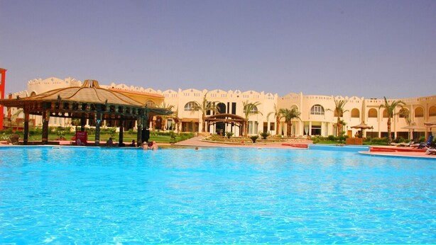A large swimming pool with a gazebo and a building with arched windows and palm trees in the background.