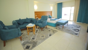 A hotel room with a bed, two blue armchairs, a small table, and a patterned rug.