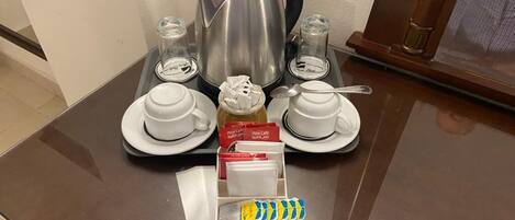 Una estación de café con una tetera, tazas y bolsitas de té sobre una mesa.