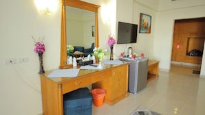 A hotel room with a wooden desk, a mirror, a television, and a small kitchenette.