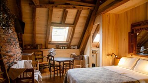 Een knus houten huisje met een slaapkamer op de zolder, een eethoek en een bakstenen muur.