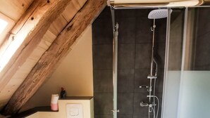 Een moderne badkamer met een glazen douchecabine, een wit toilet en een houten plafond.