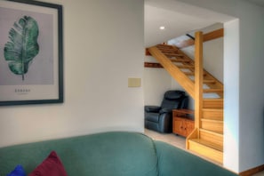 A living room with a green sofa, a framed botanical print, a black leather chair, and a wooden staircase. - Bella Vista - Bicheno Accommodation (Bicheno)