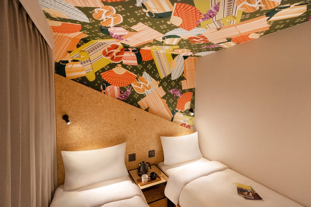 Hotellihuone, jossa on kaksi sänkyä, puinen sohvapöytä ja värikäs seinämaalaus katossa.