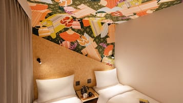 Ein Hotelzimmer mit zwei Betten, einem Holztischchen und einem farbenfrohen Wandgemälde an der Decke.