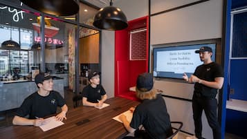 A modern meeting room with a presentation screen, wooden tables, and a red accent wall.