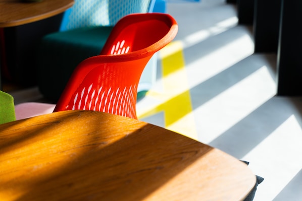 A close-up of a red plastic chair with a wooden table in the foreground. - lyf Tenjin Fukuoka (Fukuoka)