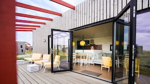 A modern outdoor deck with a glass door leading to a dining area with a table and chairs. - Chic Stay Near North Sea (Callantsoog)
