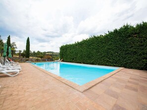 A swimming pool with lounge chairs and umbrellas, surrounded by a hedge and stone walls. - Belvilla by OYO Villa Mulinaccino (Fabro)