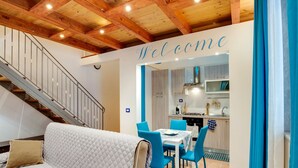 A modern interior with a staircase, a living area with a sofa and chairs, and a kitchen area with a 'Welcome' sign. - Cozy Apartment in Siracusa near Sea & City Center (Syracuse)