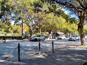 A paved walkway with a chain barrier, trees, and parked cars. - Cozy Apartment in Siracusa near Sea & City Center (Syracuse)