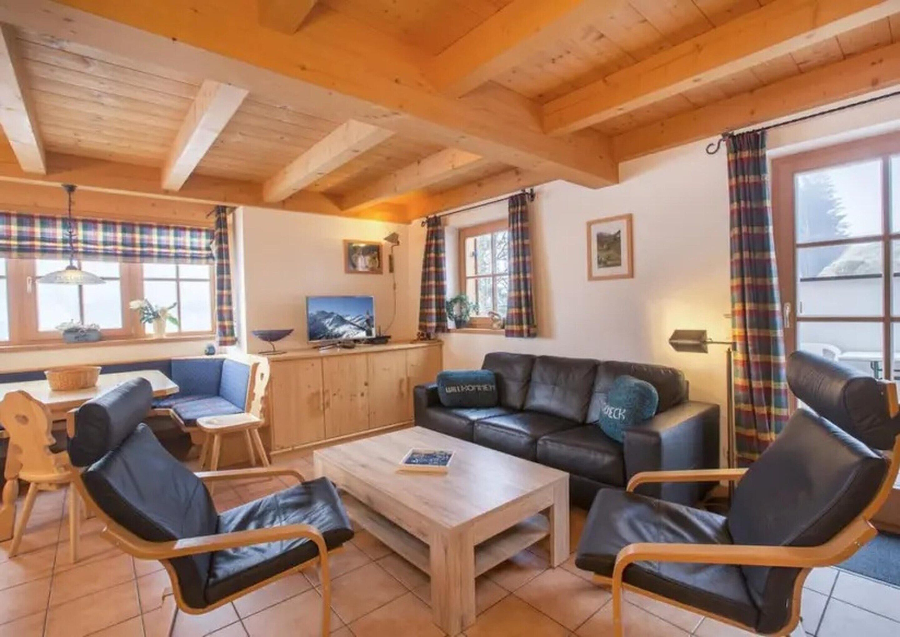 Ein gemütliches Wohnzimmer mit Holzbalkendecke, einer Couch, einem Couchtisch und einem Fernseher.