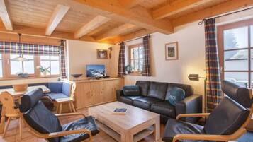 Ein gemütliches Wohnzimmer mit Holzbalkendecke, einer Couch, einem Couchtisch und einem Fernseher.