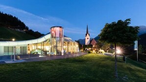 A modern building with a glass facade, a prominent cylindrical structure, and a church in the background. - Ideal Chalet in Wald-Königsleiten with Sauna near Ski Lift (Wald im Pinzgau)