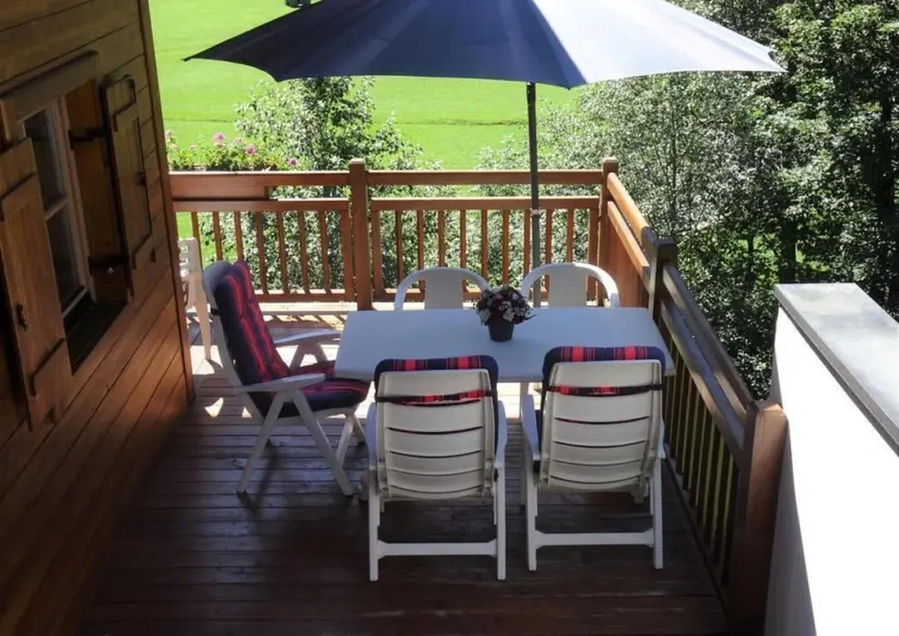 Een houten terras met een tafel, stoelen, een blauwe parasol en uitzicht op een groen gazon.