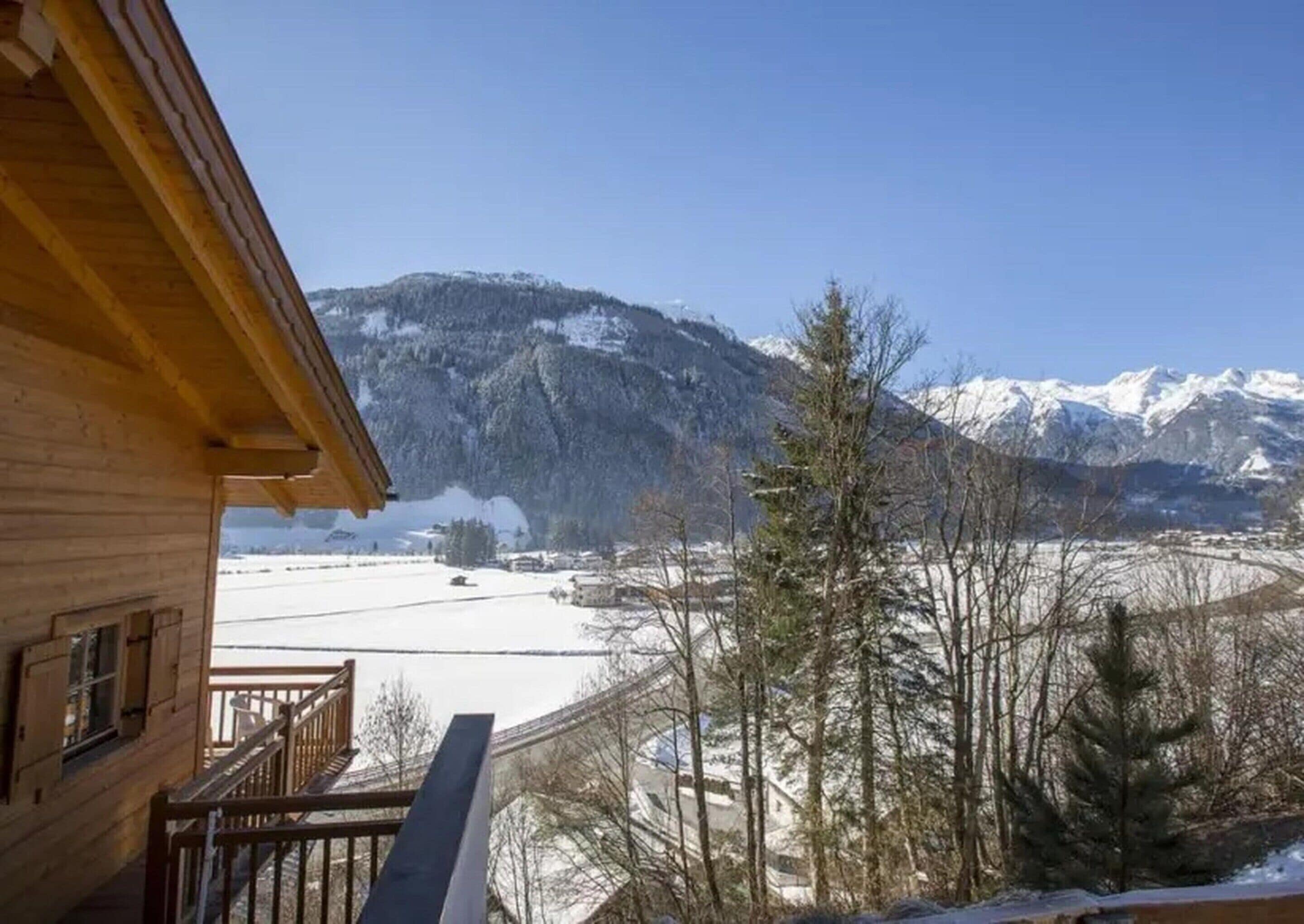 Een houten chalet met balkon, met uitzicht op een besneeuwd landschap en bergen.