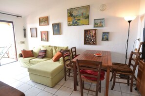 Un salon avec un canapé vert, une table à manger en bois et des chaises. Plusieurs œuvres d’art encadrées ornent le mur.