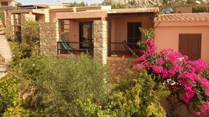 A villa with a stone facade, a balcony with a chair, and a view of rocky hills. - Belvilla by OYO Deligias (Trinità d'Agultu e Vignola)