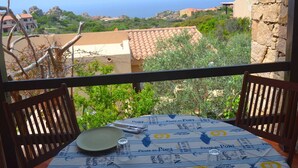 A balcony with a table set for dining, overlooking a coastal landscape with buildings and greenery. - Belvilla by OYO Deligias (Trinità d'Agultu e Vignola)