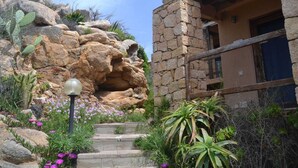 A stone building with a staircase leading to a door, surrounded by cacti and desert plants. - Belvilla by OYO Deligias (Trinità d'Agultu e Vignola)