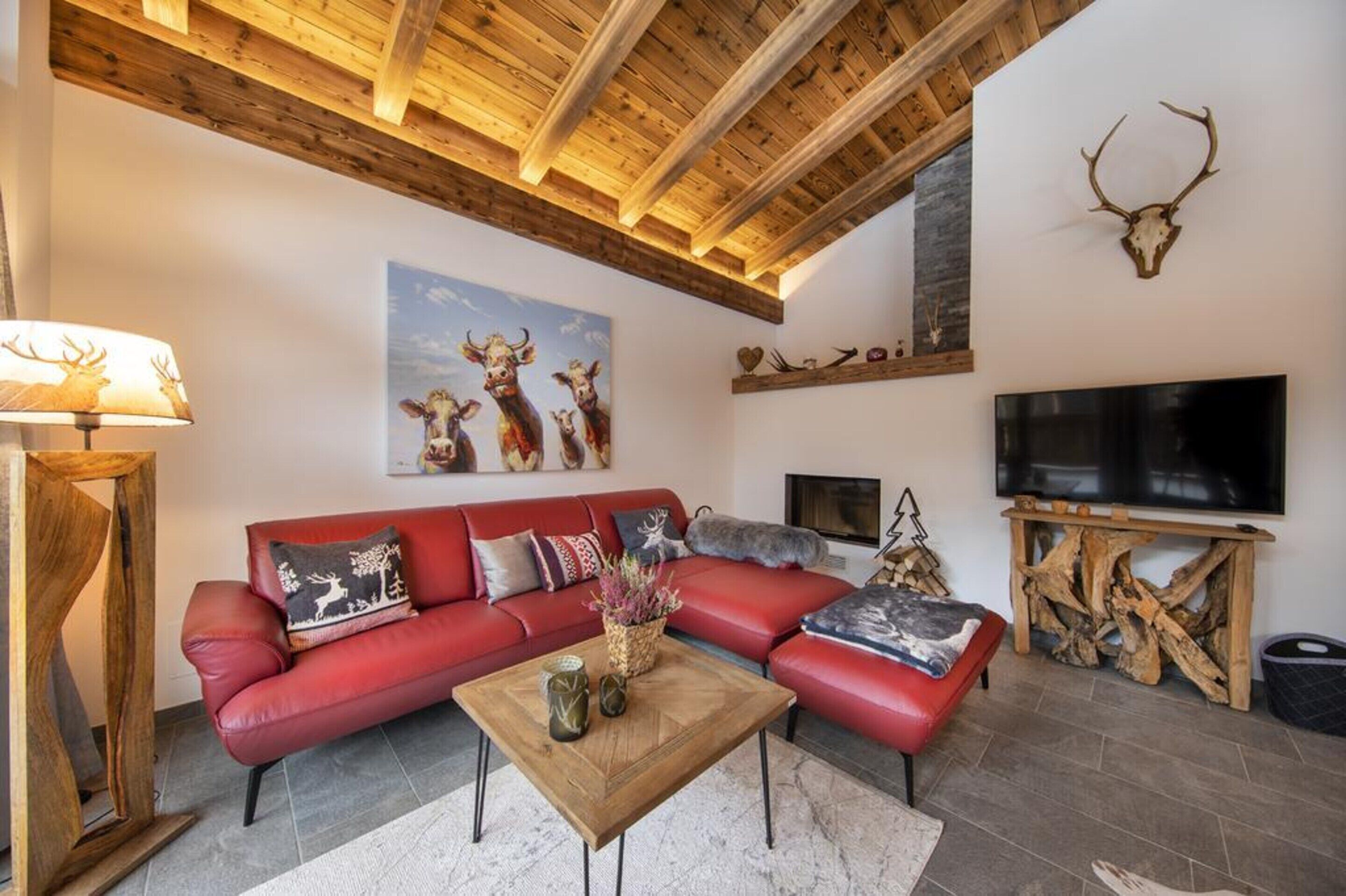 A living room with a red sofa, wooden coffee table, and a mounted deer skull on the wall.