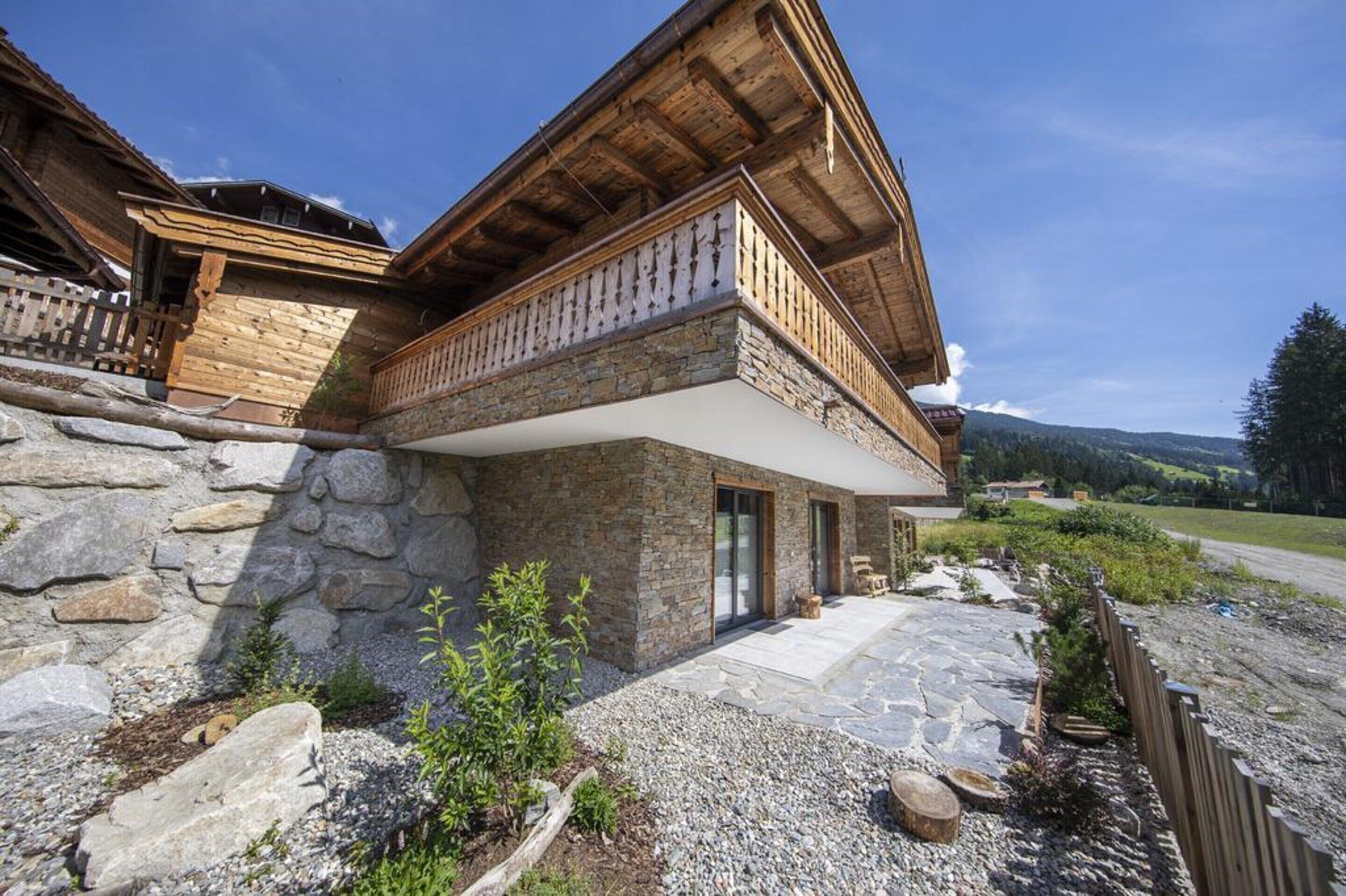 Ein Steinhaus mit einem hölzernen Balkon, einem Steinweg und Blick auf die umliegende Landschaft.