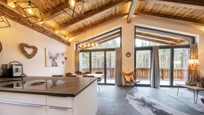A modern kitchen with a large island, wooden ceiling beams, and large windows offering a view of the forest. - Ornate Chalet in Neukirchen near Wildkogel Ski Arena (Neukirchen am Grossvenediger)