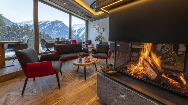A modern living room with a fireplace, large windows, and a view of snow-capped mountains. - Ornate Chalet in Neukirchen near Wildkogel Ski Arena (Neukirchen am Grossvenediger)