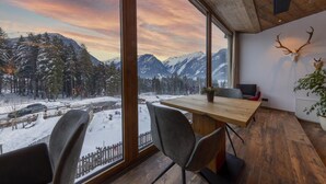 A room with a large window offering a view of snow-covered mountains and a forest. There is a wooden table and two chairs. - Ornate Chalet in Neukirchen near Wildkogel Ski Arena (Neukirchen am Grossvenediger)