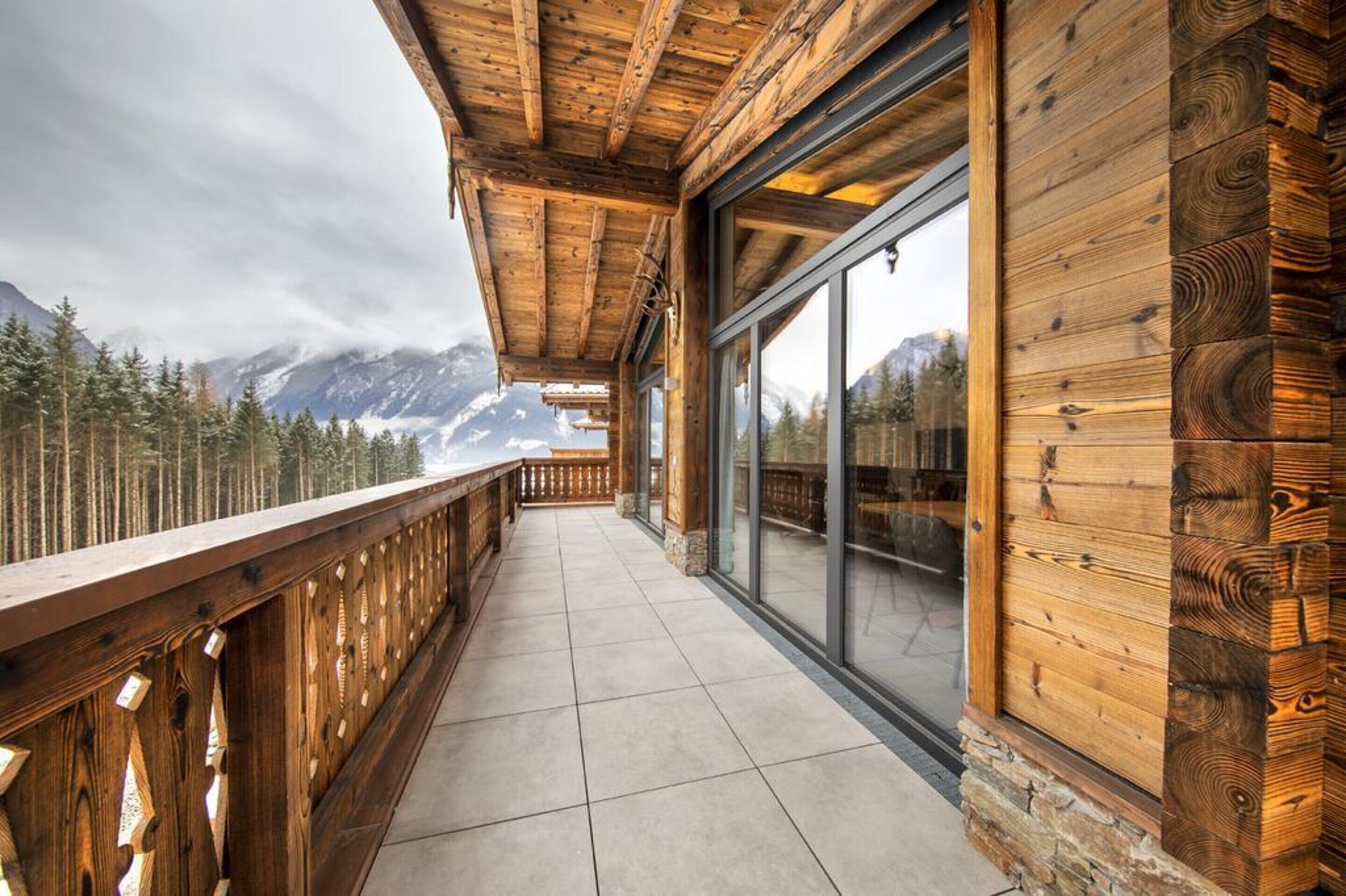 A wooden balcony with a view of snow-capped mountains and pine trees.