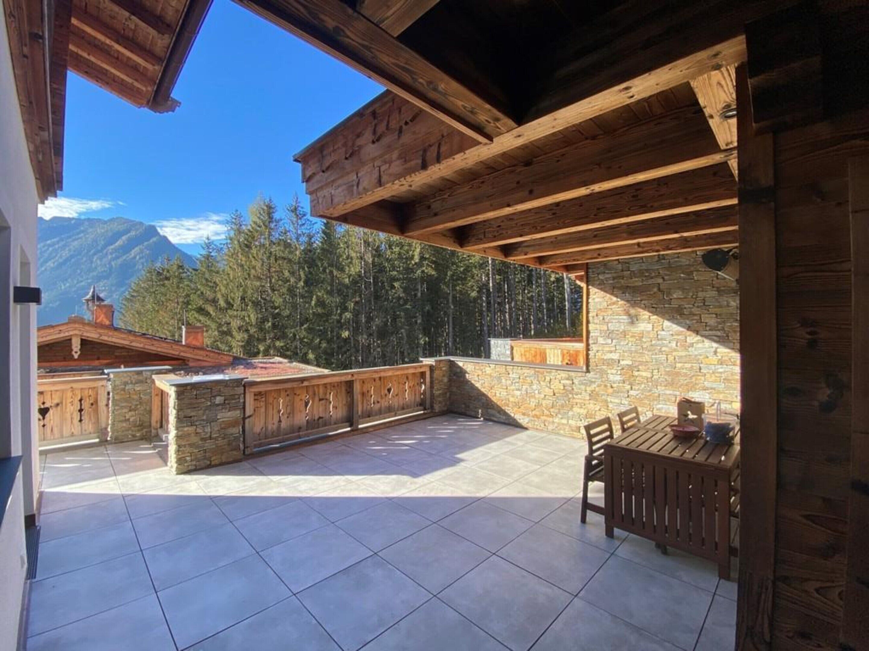A wooden deck with stone walls, a table, and chairs.