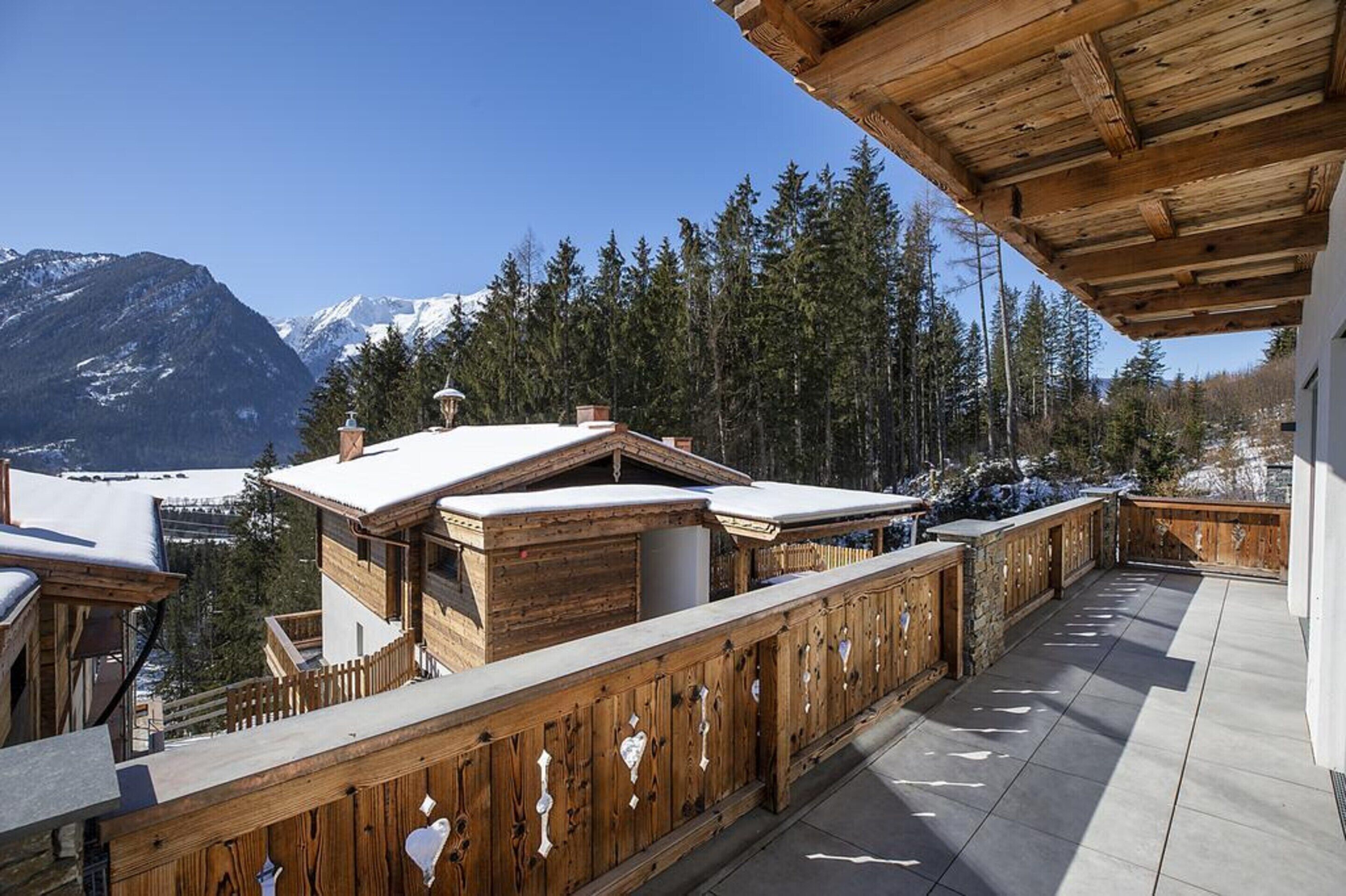 Una terraza de madera con vistas a montañas nevadas y pinos.