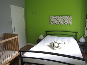 A bedroom with a bed, a crib, a green wall, and a painting.