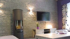 A modern living room with a stone wall, a flat-screen TV, a fireplace, a dining table, and a sofa. - Luxurious Countryside Holiday Home With Garden (Malmedy)