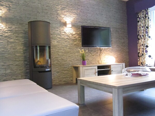 A modern living room with a stone wall, a flat-screen TV, a fireplace, a dining table, and a sofa.