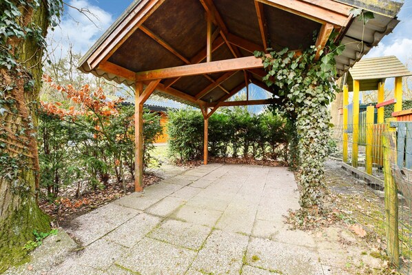 Un patio cubierto con suelo de baldosas, rodeado de vegetación y una cerca de madera.